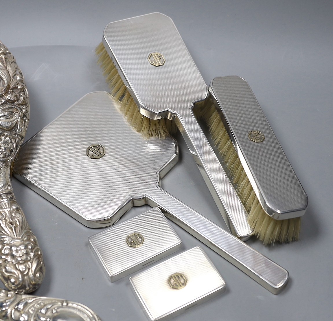 A 1970's engine turned silver three piece dressing table set, with a pair of matching jar lids, and a repousse decorated three piece dressing table set